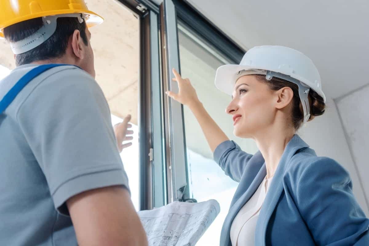 Eine Bausachverständige überprüft die Fenster mit Handwerker