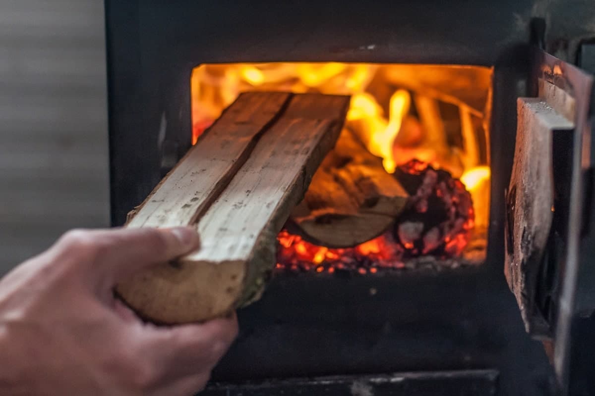 Mann, der Holz in Kaminofen nachlegt