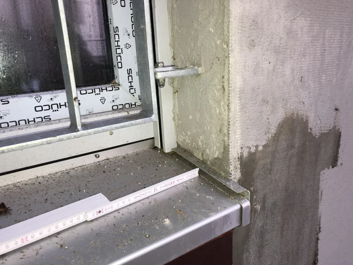 Eine mit Armierungsmörtel verschmutzte Aluminiumfensterbank. Während der Außenputz ausgeführt wird, ist die Fensterbank nicht geschützt.