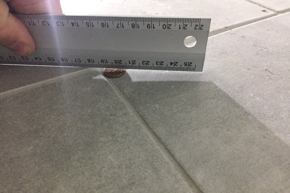 Ein Fliesenüberzahn wird mit einem Winkel und einer 1-Cent-Münze überprüft.-min