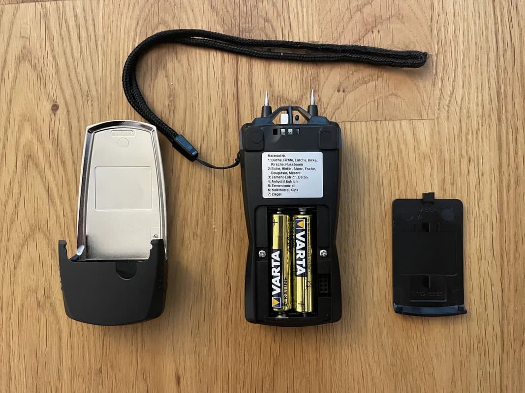 Das Material- und Holzfeuchtigkeitsmessgerät Testo 606-2, mit geöffnetem Batteriefach, in dem zwei AAA-Batterien zu sehen sind.