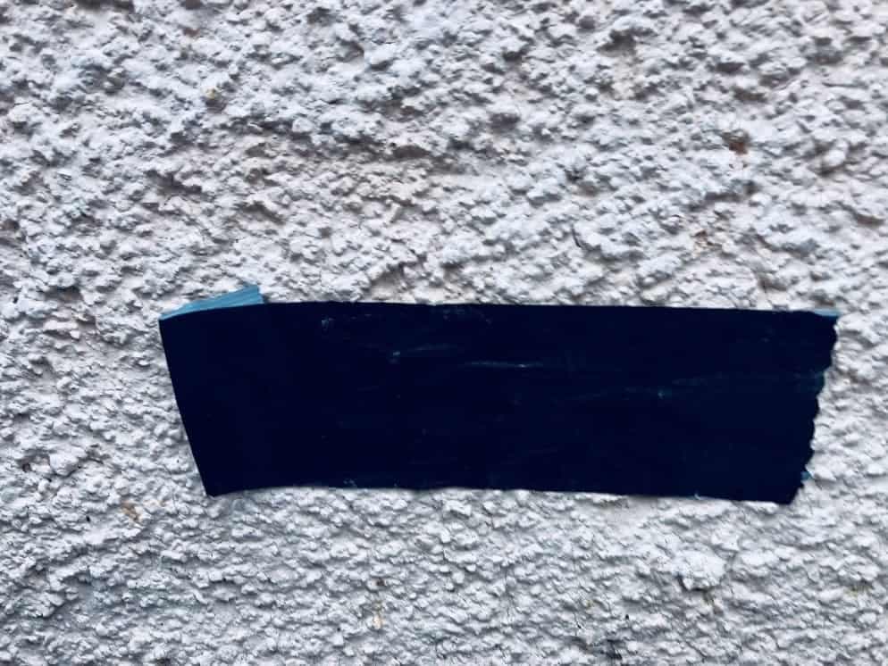 Ein Klebeband auf einer Putzfassade, um zu prüfen, ob der alte Anstrich noch hält.