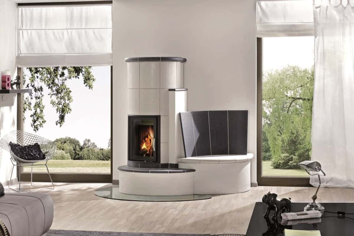 Ein moderner Kachelofen mit Sitzbank. Durch eine große Sichtscheibe ist das Feuer zu sehen Durch helle Keramikplatten und zeitlos schlichtes Design passt der Kachelofen gut zum Stil der Einrichtung und ist ein echter Hingucker.